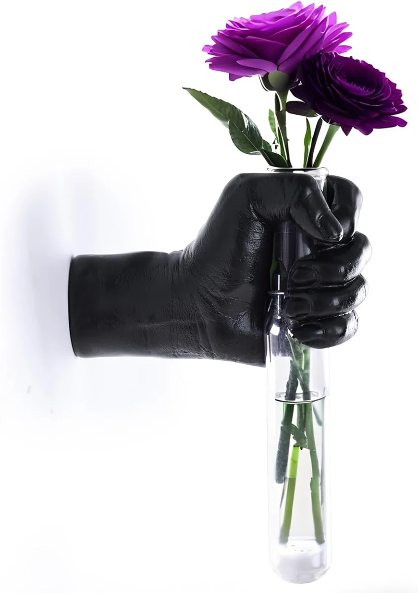 Matte black wall-mounted sculpture shaped like a life-size human hand emerging from the wall, holding a row of clear glass test tubes used as tiny vases for propagating plants or holding single-stem flowers